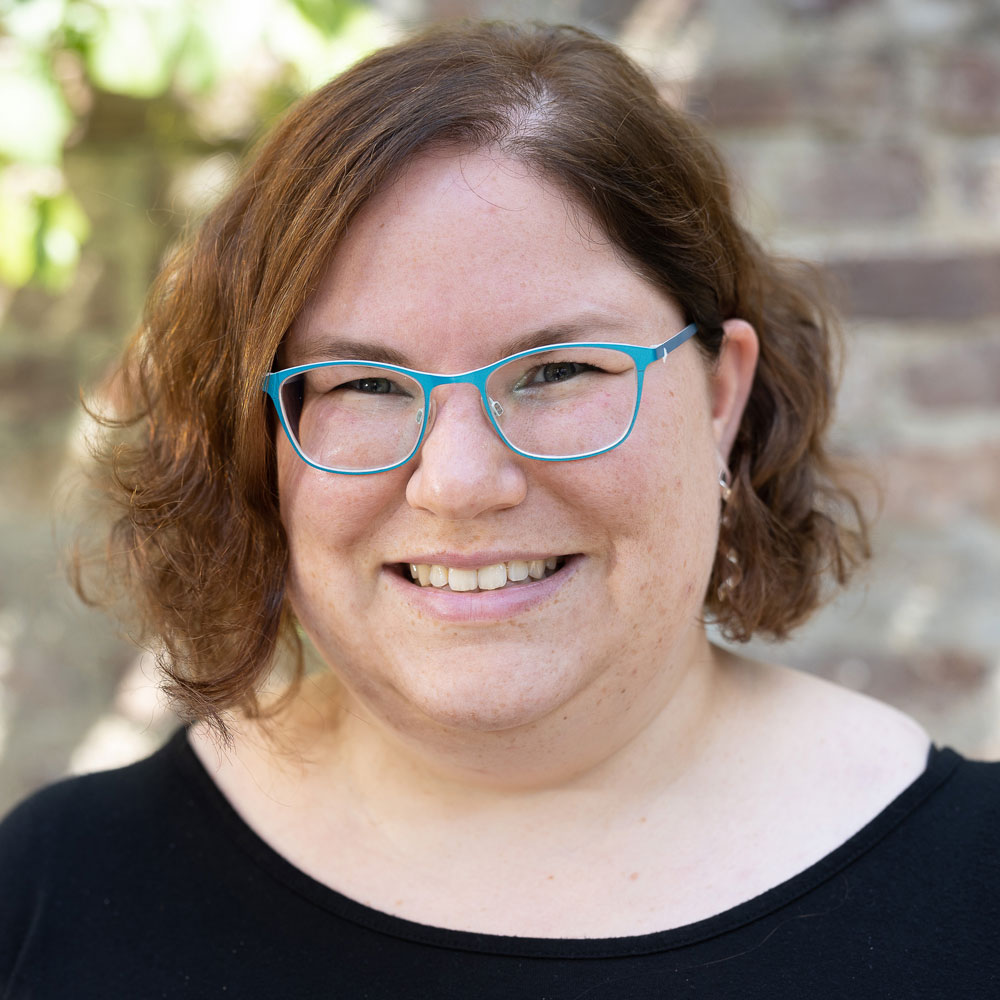 Eine Frau mit halblangen Haaren und Brille lächelt in die Kamera.
